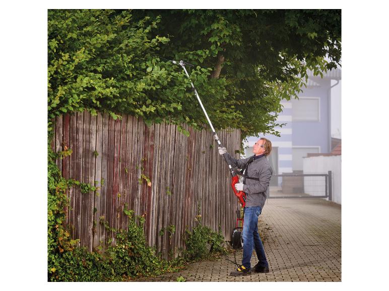 Mann schneidet Hecke mit einer Langstiel-Heckenschere an einem Holzzaun.