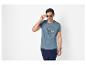 Mann in blauem T-Shirt mit maritimem Aufdruck, dunkelblauer Hose und Sonnenbrille.