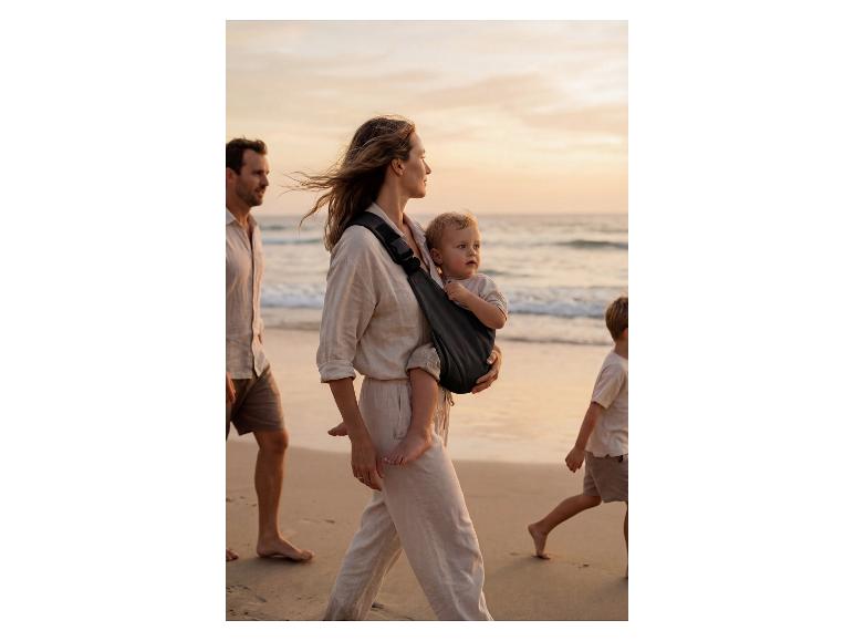 Mutter mit Baby in FILLIKID Babytrage am Strand mit Familie.