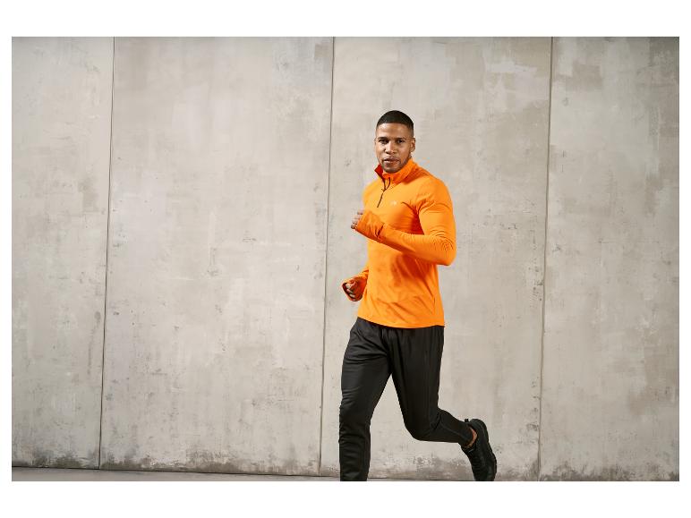 Ein Mann trägt eine orangefarbene Trainingsjacke und schwarze Jogginghose beim Laufen.
