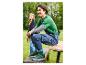 Mann in grünem T-Shirt und Jeans-Latzhose, grüne Sneaker tragend, sitzt auf einer Holzbank.