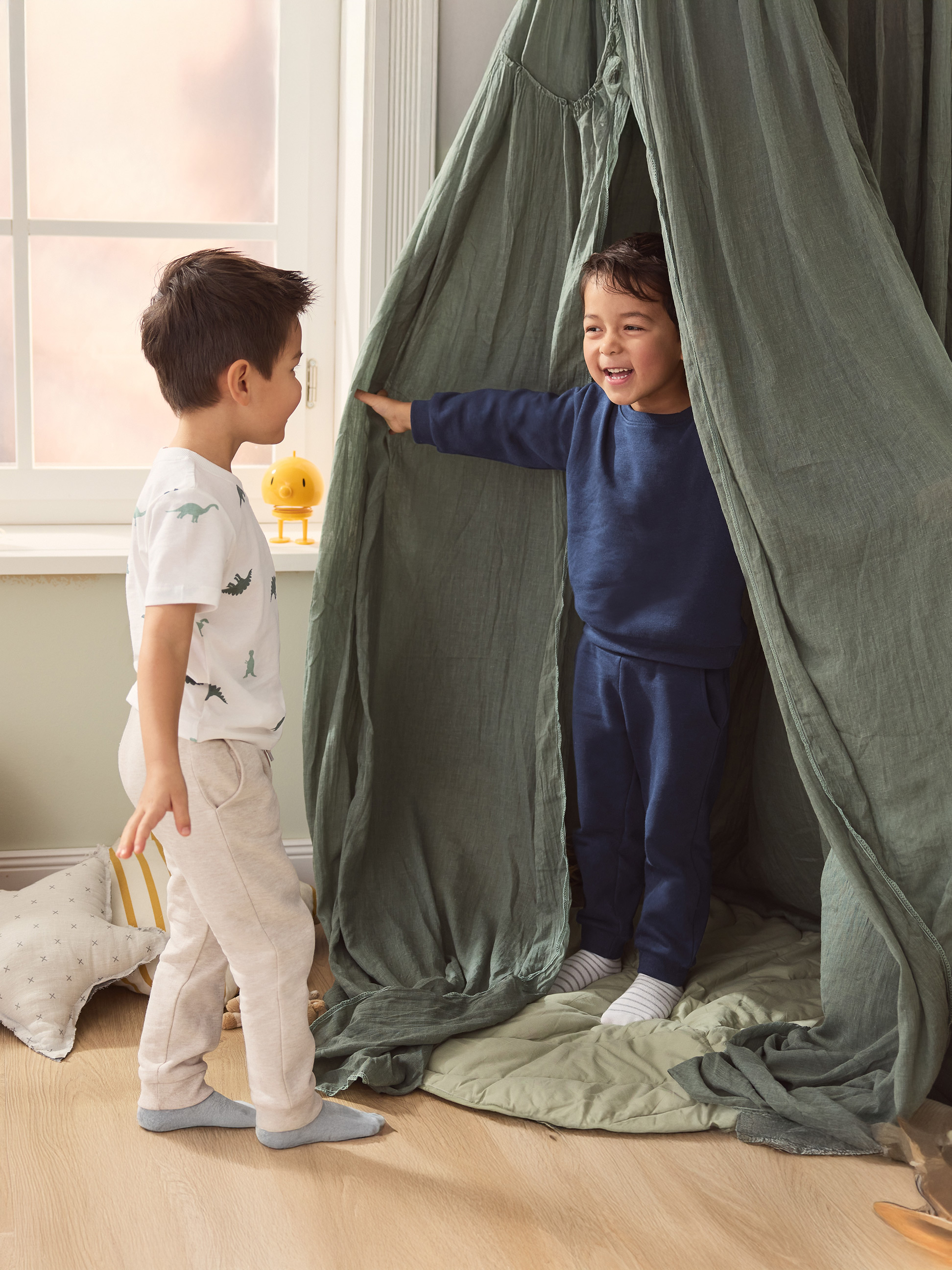 Zwei Jungen spielen in einem grünen Spielzelt, einer trägt ein Dinosaurier-T-Shirt.