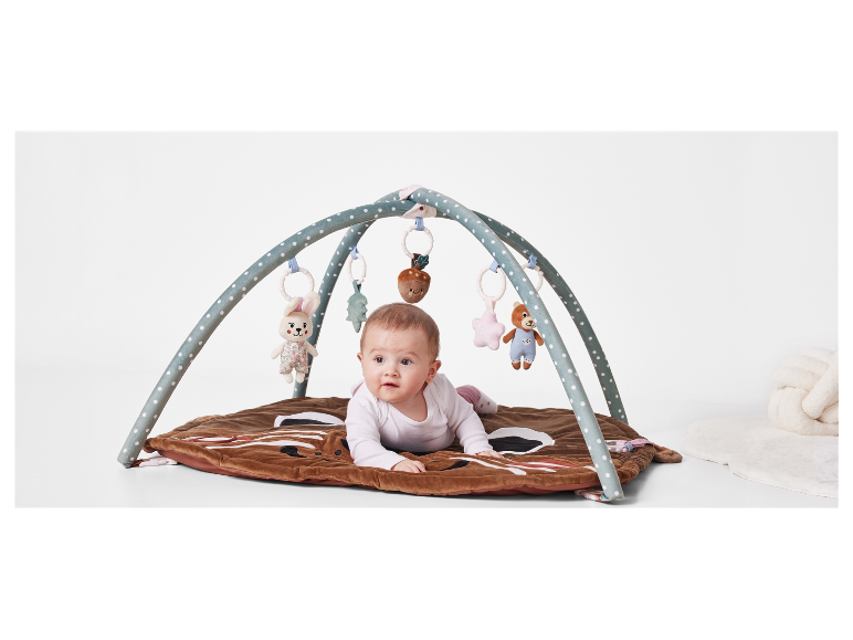 Baby liegt auf einer Spielmatte mit Baldachin.