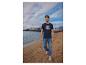 Mann in marineblauem T-Shirt und Jeans an einem Sandstrand.