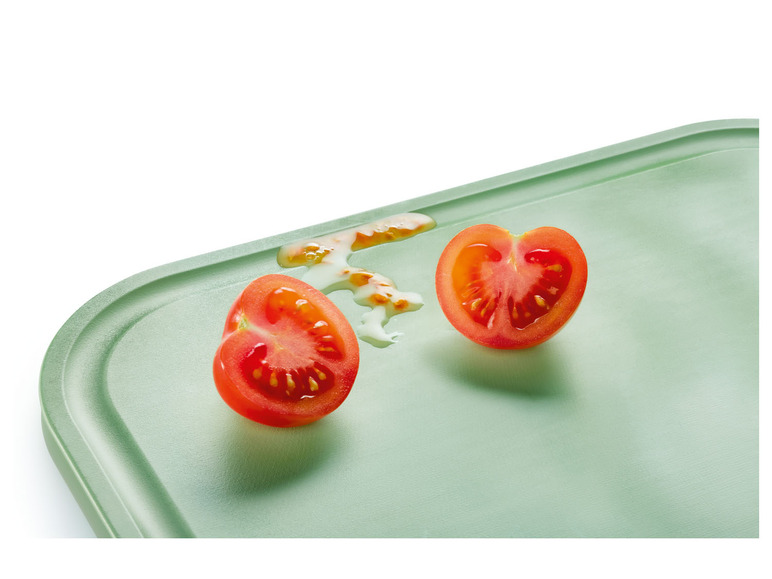 Zwei Tomatenhälften auf einem grünen Schneidebrett.