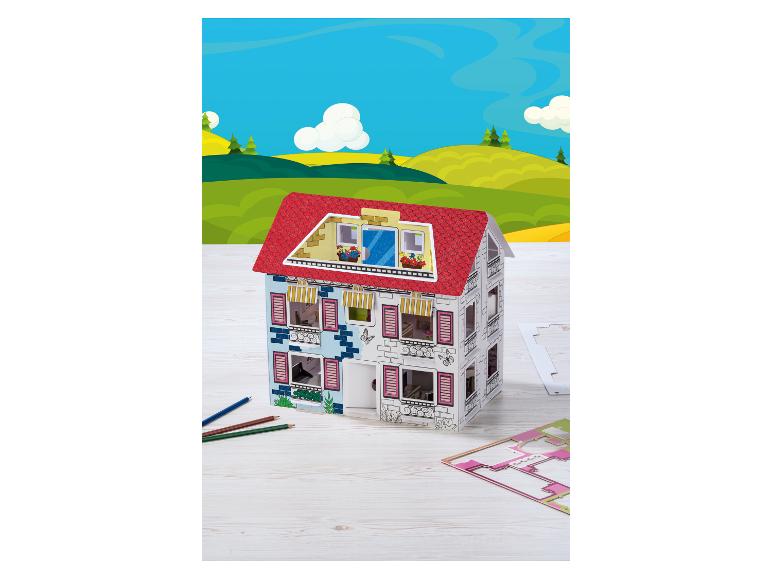 Karton-Puppenhaus mit rotem Dach, Buntstifte und eine Stanzform auf einem Holztisch.