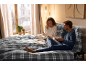 Ein Paar in gemütlichen Pyjamas frühstückt im Bett mit grau karierter Bettwäsche.
