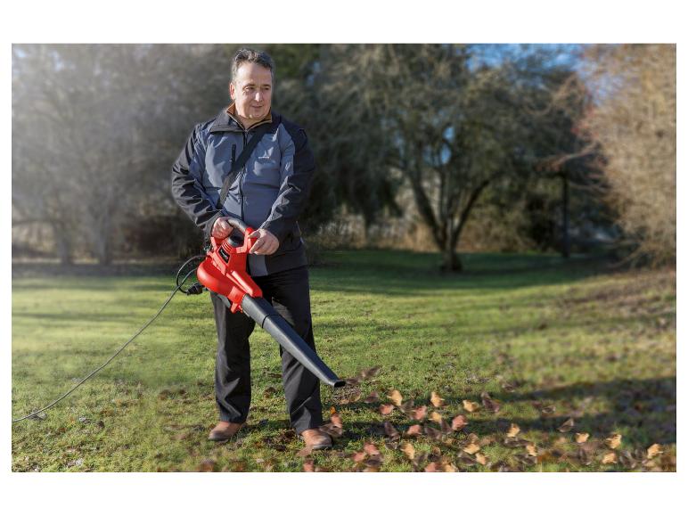 Mann benutzt einen elektrischen Laubbläser auf einem Rasen mit Herbstlaub.