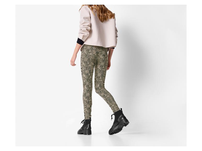 Frau in beiger Jacke und gemusterten Leggings, mit schwarzen Stiefeln