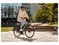 Lächelnde Frau mit Helm und Sonnenbrille fährt E-Bike durch einen Stadtpark.