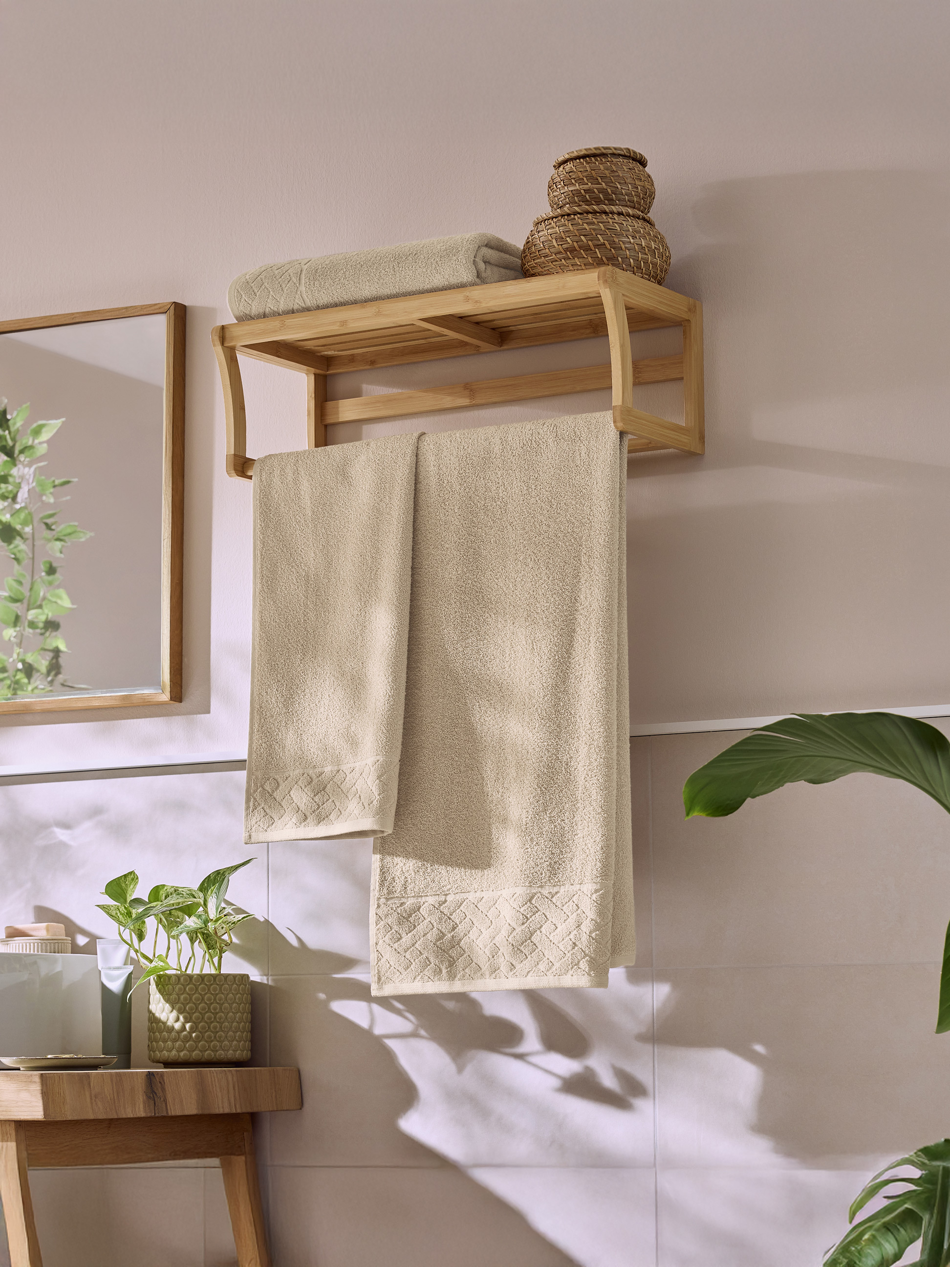 Badezimmer mit einem Handtuchhalter aus Holz, beigen Handtüchern und grünen Pflanzen.