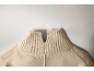 Nahaufnahme eines beigen Strickpullovers mit hohem Rippkragen und kleinem V-Ausschnitt.