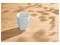 Weiße Tasse auf einem Holztisch mit Blattschatten.