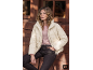 Frau in cremefarbener Steppjacke, rosa Langarmshirt und dunkler Jeans, sitzt draußen.