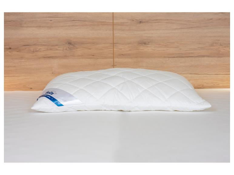 Weißes gestepptes Kissen auf einem Bett mit Holzkopfteil.