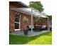 Graue Terrassenpergola mit transparentem Dach über einem Outdoor-Loungebereich mit Möbeln und Pflanzen.