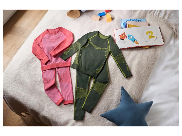 Zwei Sets Kinder-Thermo-Unterwäsche, eines rosa und eines grün, auf einer Decke mit Spielzeug.