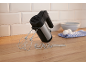 Handmixer mit Rührbesen und Knethaken, Eier und Schüssel auf einer Holztheke.