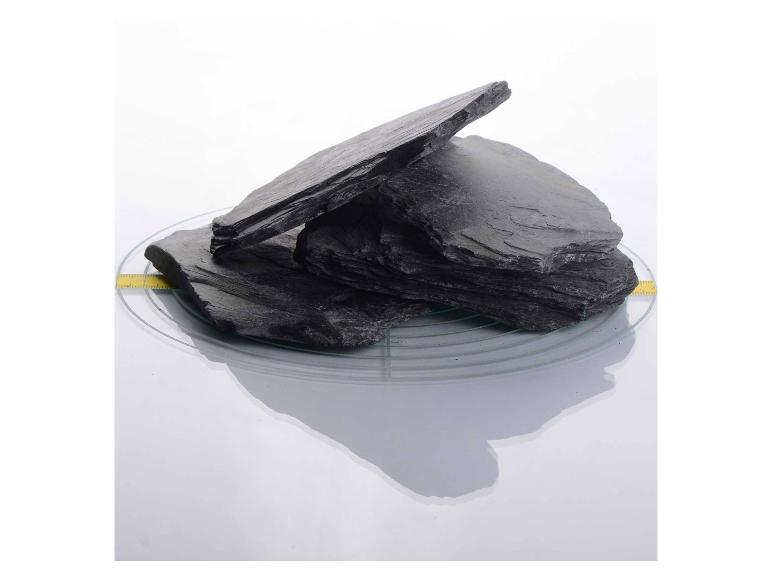 Mehrere Stücke dunkler Schieferstein auf einer klaren Glasplatte mit Maßband