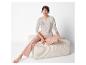 Eine Frau in einem beigen Pyjama mit dem Aufdruck 'Sleep Dream Relax' sitzt auf einem hellen Hocker.