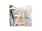 Heller Holzhochstuhl mit Tablett, neben einem Tisch mit Kindergeschirr.