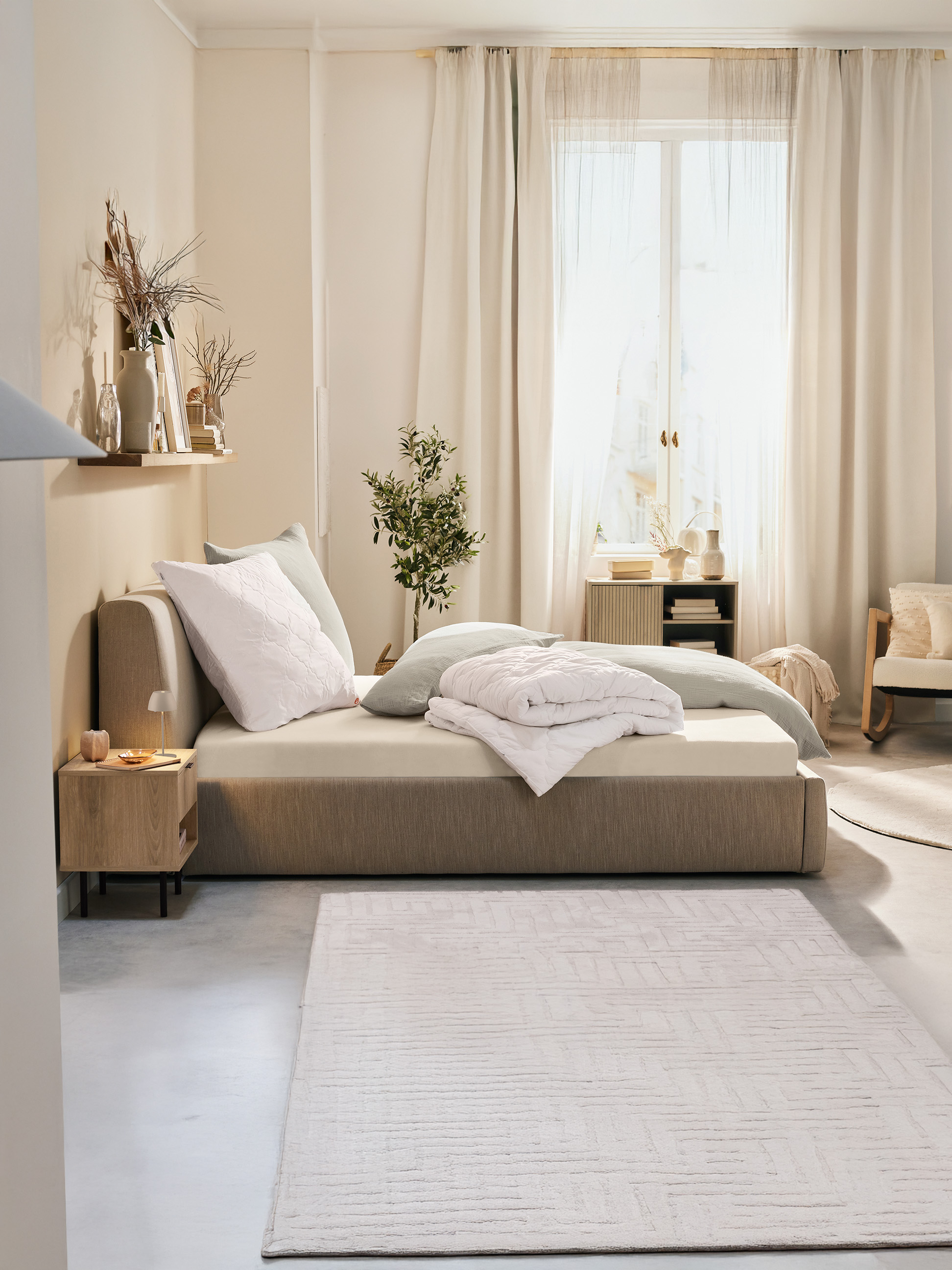 Helles Schlafzimmer mit Polsterbett, Nachttisch aus Holz und cremefarbenem Teppich.