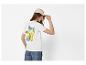 Frau in weißem T-Shirt mit Zitronen und „La Dolce Vita“-Aufdruck auf dem Rücken, beiger Kappe.