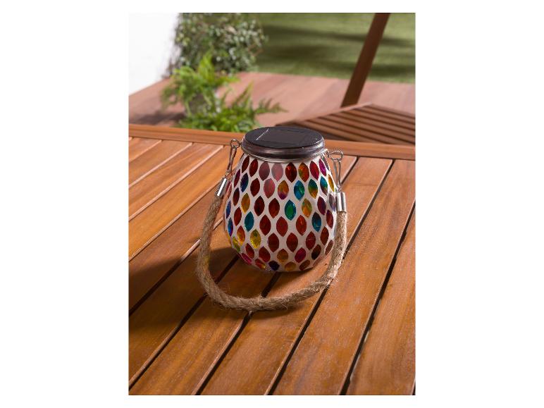 Eine bunte, runde Glaslaterne mit Solarpanel auf einem Holztisch.