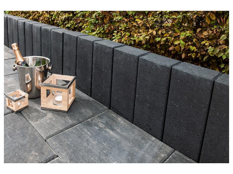 Schwarze Gartenumrandung mit Sektkühler und Kerzenhaltern auf einer Terrasse.