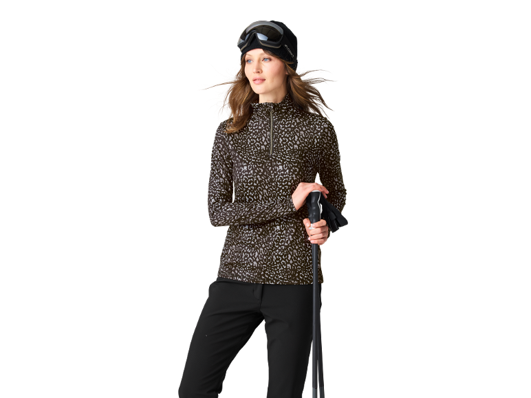 Frau im sportlichen Ski-Funktionsshirt mit Allover-Print, schwarzer Hose und Skistöcken.