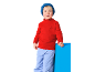 Junge in rotem Rollkragenpullover mit Kompass und blauer Hose, lehnt an blauem Block.