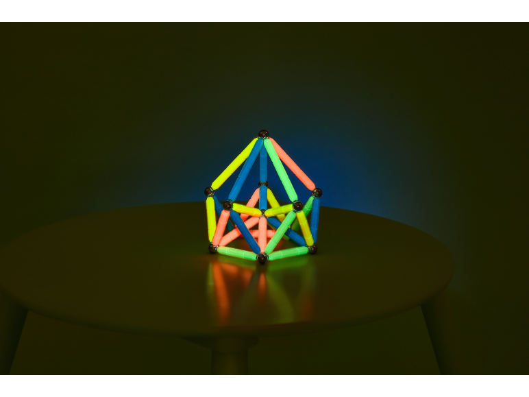 Leuchtende geometrische Konstruktion auf einem Tisch vor dunklem Hintergrund.