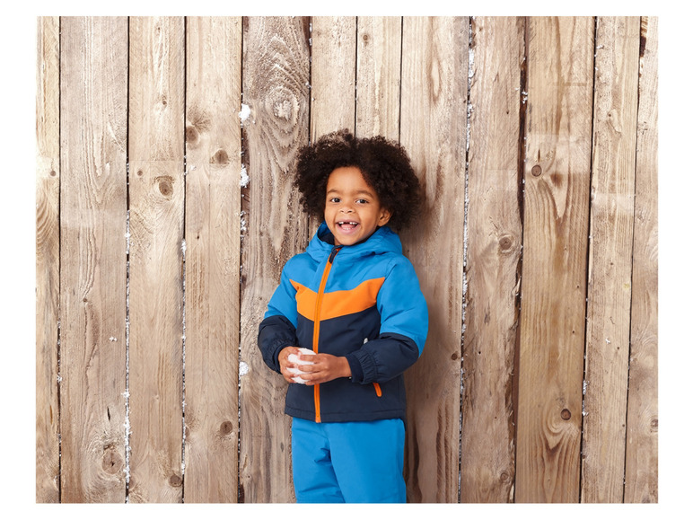 Ein Junge in einer blauen Winterjacke und Hose hält eine Schneeball.