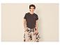 Mann in dunklem T-Shirt mit 'Resilience'-Aufdruck, beiger Hose und kariertem Hemd um die Taille gebunden.