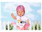 BABY born Puppe mit rosa Helm und auf einem Fahrrad, mit einem weißen Zaun im Hintergrund.