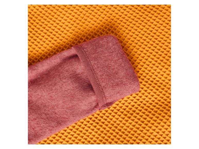 Nahaufnahme einer gefalteten rosa Fleecedecke auf einer gelben Waffelstoffoberfläche.