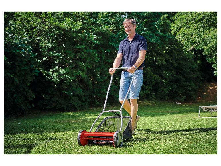 Mann mäht Rasen mit einem Handrasenmäher in einem Garten.