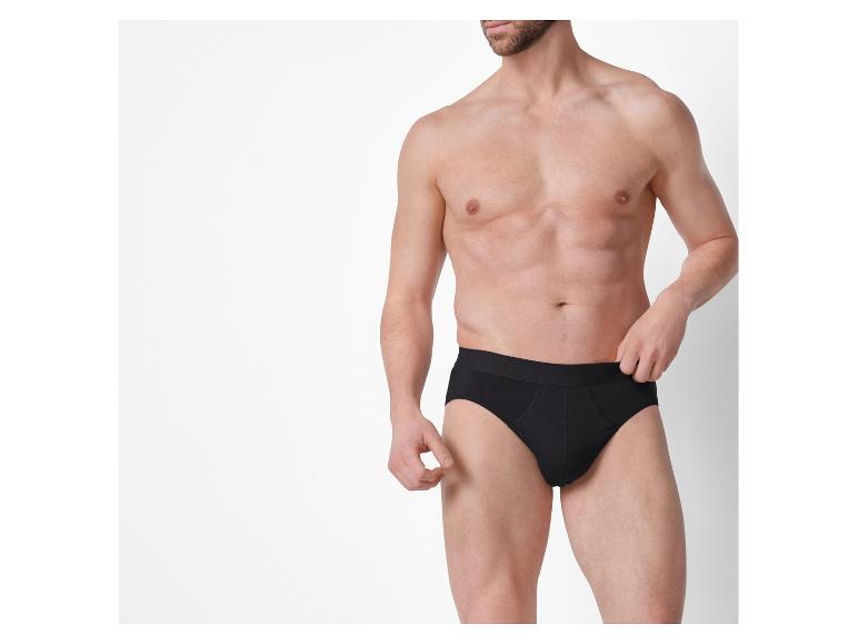 Hemdloser Mann in schwarzen Slips vor weißem Hintergrund.