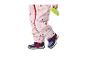 Kind in rosa Regenanzug mit Herzchenmuster und dunkelblauen Schuhen, hält ein grünes Spielzeug.