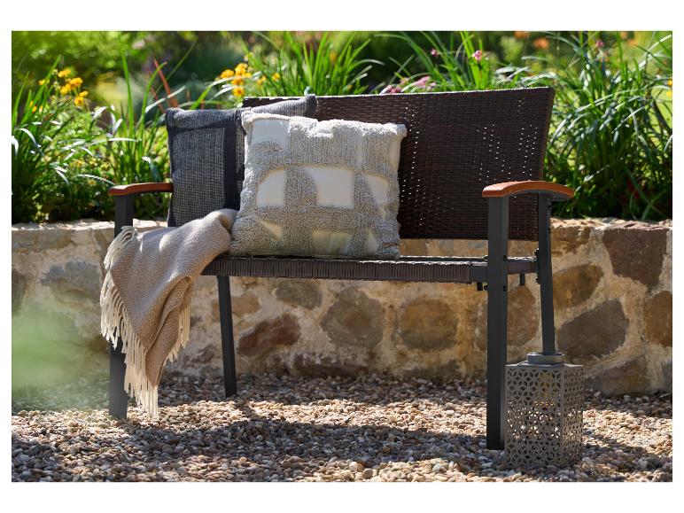 Gartenbank mit Kissen und Decke, vor Grün und einer Steinmauer.