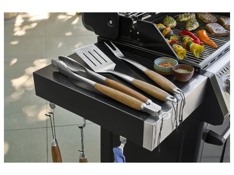 Grill mit Grillbesteck, Gewürzen und gegrillten Fleisch- und Gemüsespießen.