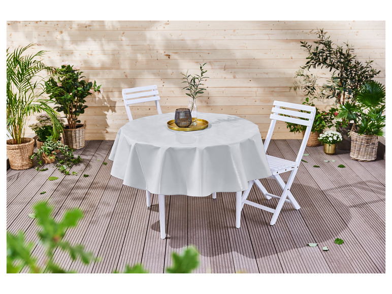 Eine weiße runde Tischdecke auf einer Holzterrasse mit zwei weißen Stühlen.