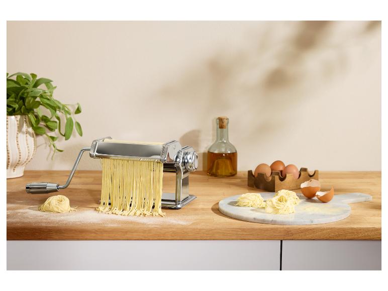 Nudelmaschine mit frischer Pasta, Eiern und Olivenöl auf einer Holzarbeitsplatte.