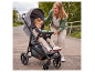 Lächelnde Frau mit Kleinkind in grauem Kinderwagen im Freien.