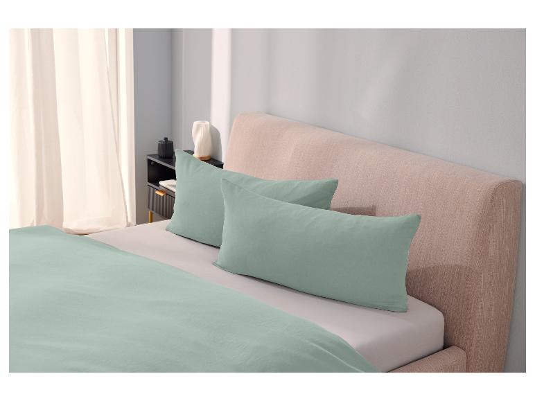 Bettwäsche und Kissen in grün-grau auf einem beigen Bett.