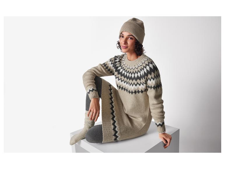 Frau in langem Fair Isle Pullover und beiger Mütze, sitzend.