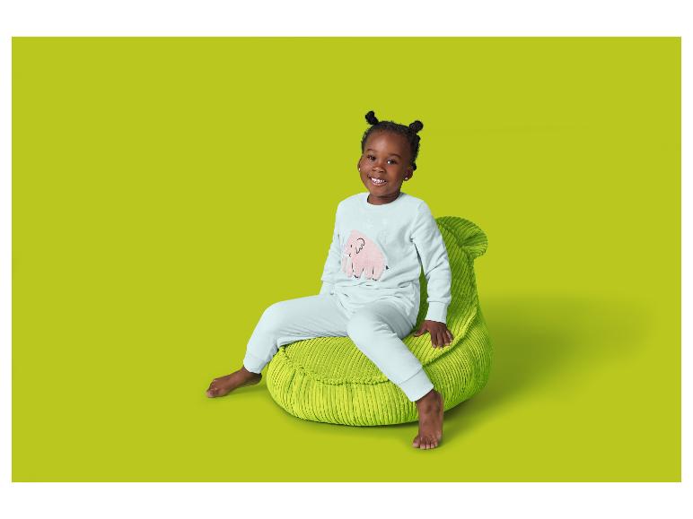 Ein lächelndes Mädchen sitzt auf einem grünen Sitzsack und trägt einen hellen Pyjama mit einem rosa Elefanten.