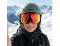 Person mit Skihelm und Skibrille, die schneebedeckte Berge reflektiert, lächelt an einem sonnigen Tag.