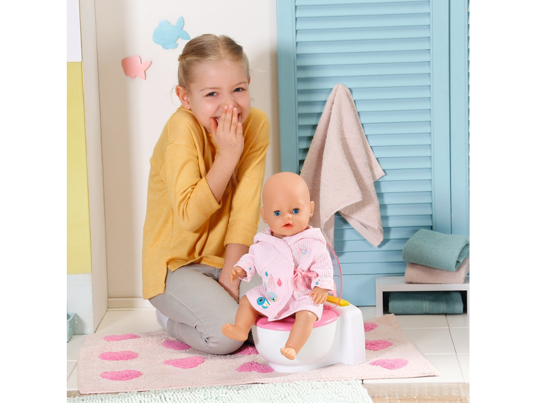 Lachendes Mädchen mit Puppe auf einem Töpfchen, in einer Badezimmerumgebung.