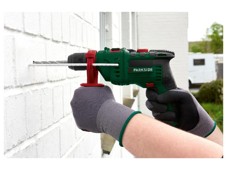 PARKSIDE Schlagbohrmaschine bohrt in eine weiße Wand, gehalten von behandschuhten Händen.